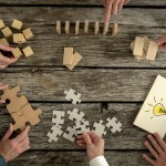Businessmen planning business strategy while holding puzzle pieces, creating ideas with light bulb drawn on paper and rearranging wooden blocks. Conceptual of teamwork, strategy, vision or education.